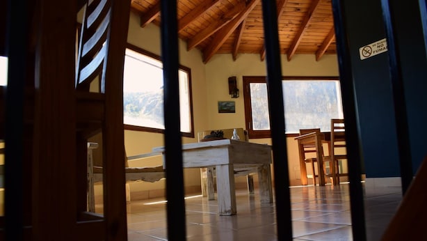 A room with a wooden ceiling, a dining table, and chairs. There is a window with a view of mountains.
