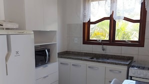 A compact kitchen with white cabinets, a microwave, a stove, and a window with a view of palm trees. - Pousada Estrela Guia (Florianópolis)