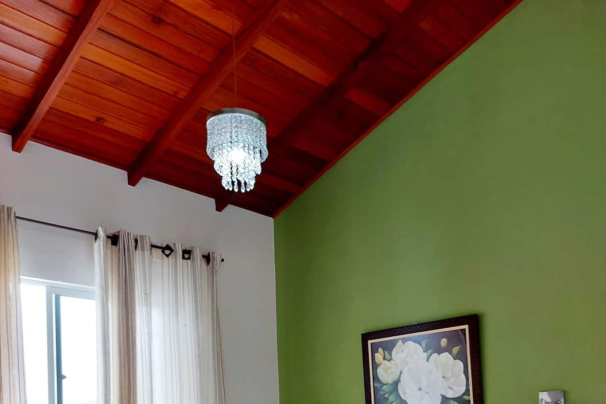 A hotel room with a bed, a chandelier, a painting, and a window with curtains.