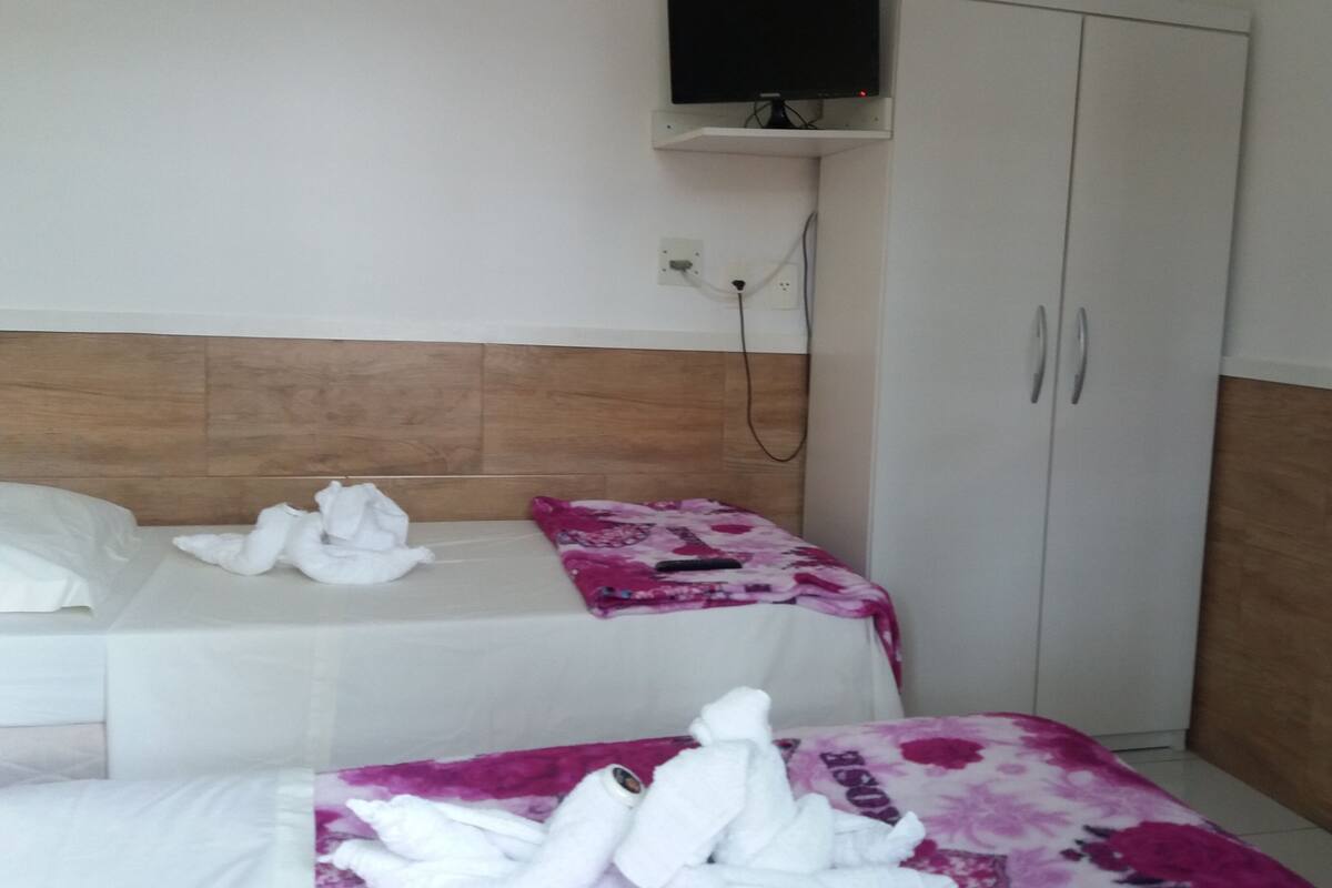 A hotel room with two beds, a wooden headboard, a wardrobe, and a television mounted on the wall.