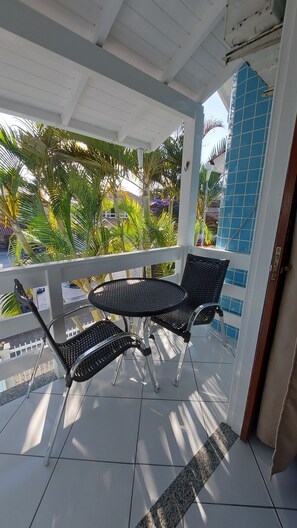 A covered outdoor seating area with two black metal chairs and a table, surrounded by a white railing, with a view of palm trees and a building in the background. - Pousada Estrela Guia (Florianópolis)