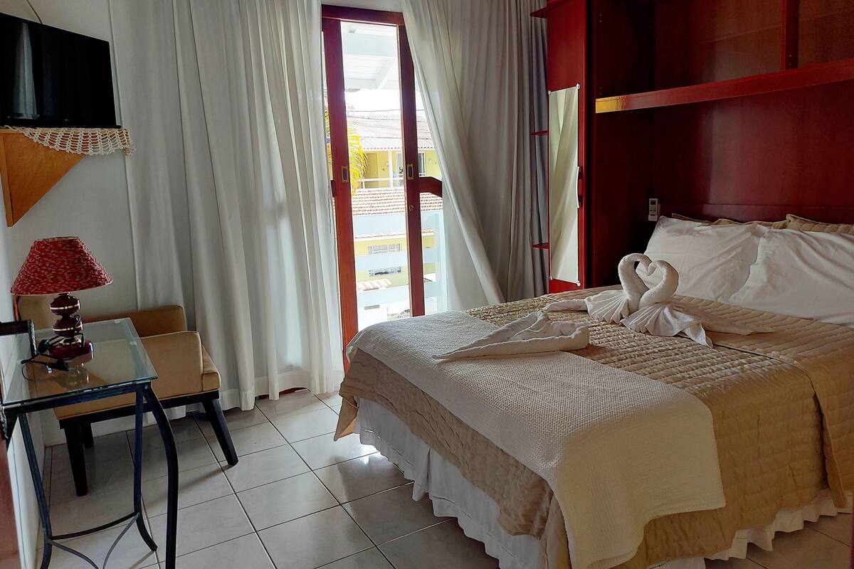 A hotel room with a bed, a desk, a lamp, and a view of the outside.