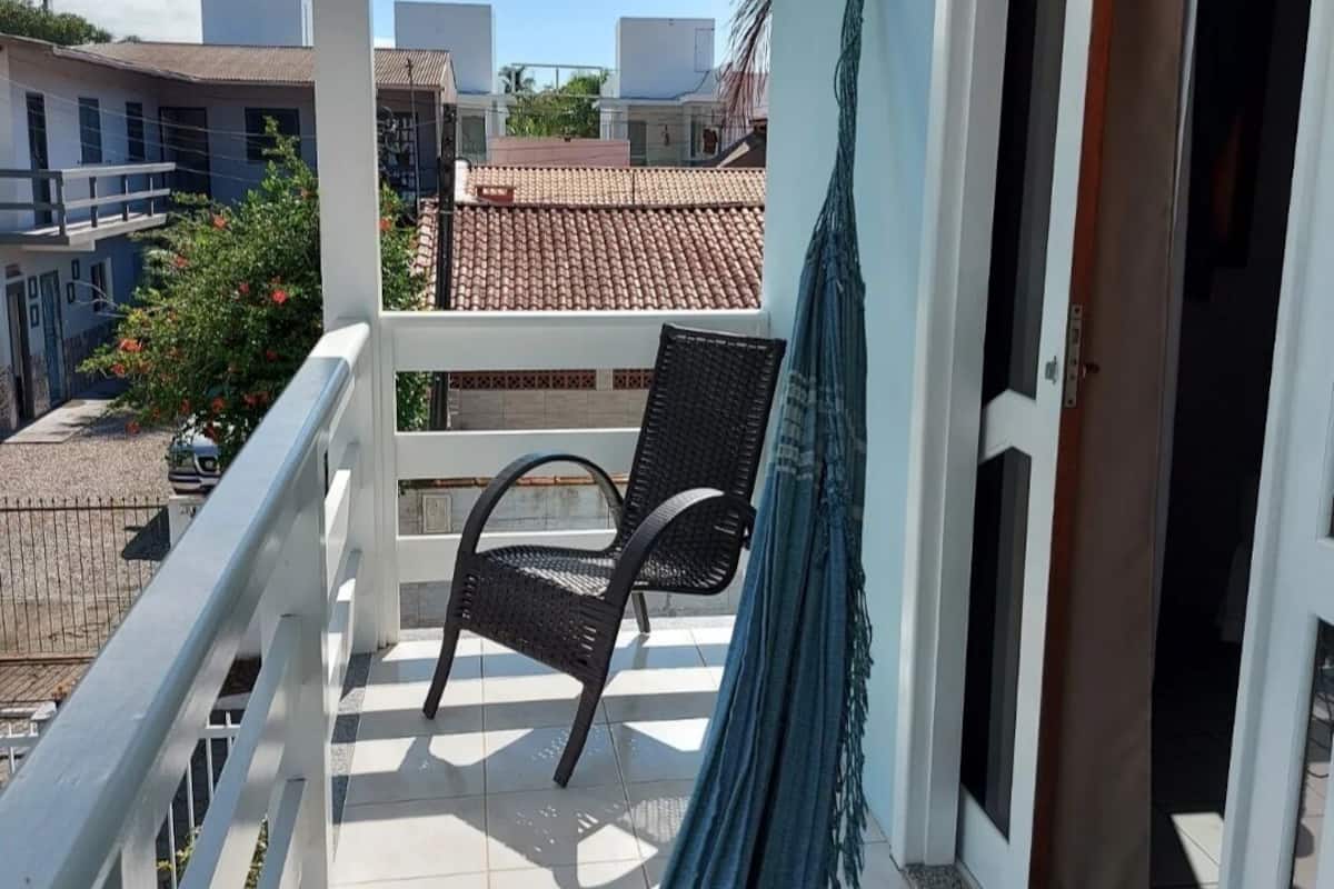 A balcony with a chair and a hammock, overlooking a residential area with tiled roofs.