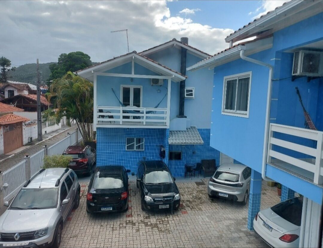 A residential building with a blue facade, a balcony, and a parking area with several cars.