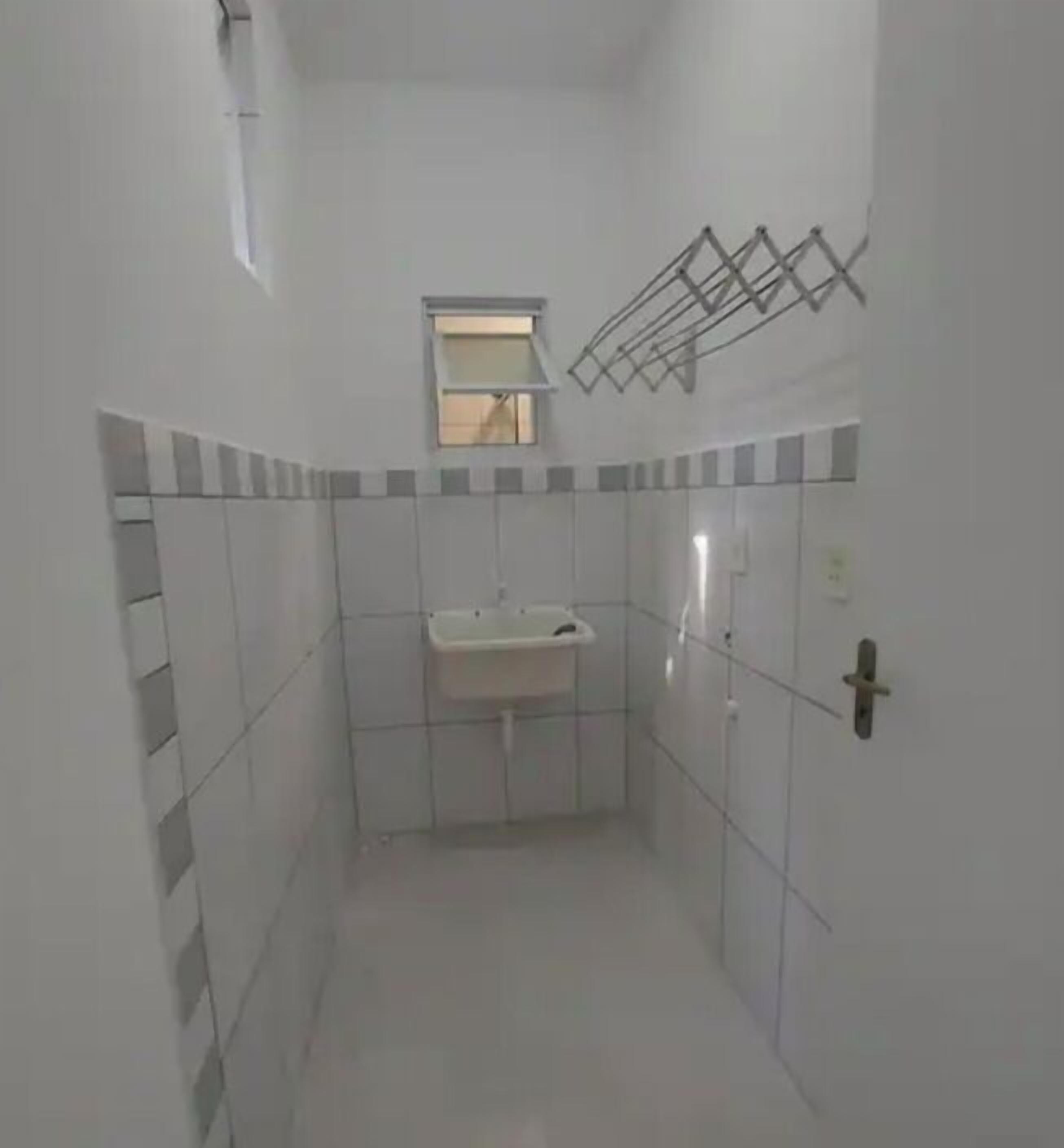 A small, narrow bathroom with white tiled walls, a single sink, and a window above it.