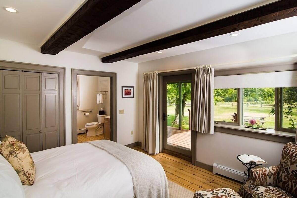 Un dormitorio con una cama grande, un baño y vistas a un jardín por una puerta corredera.