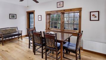 A dining area with a wooden table and chairs, a bench, and a window with a view of trees.