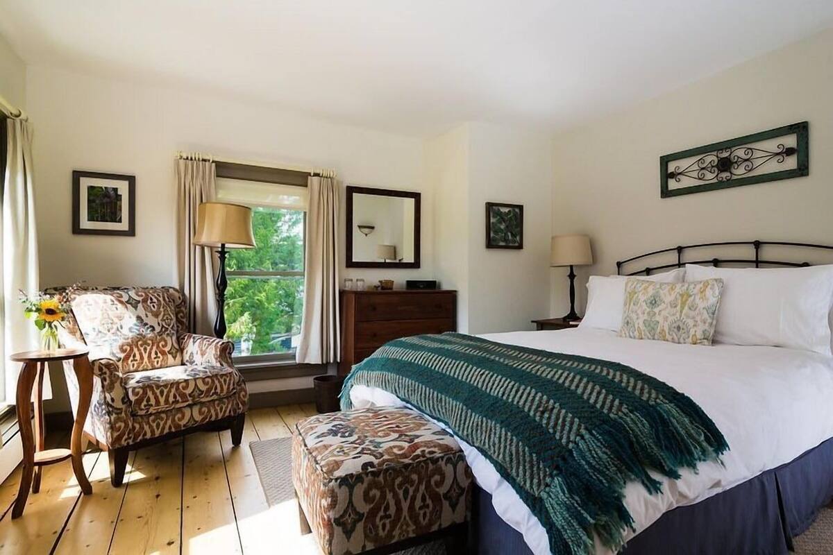 Un dormitorio con una cama grande, una silla, una mesita y un aparador.