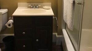 Ein Badezimmer mit einem weißen Waschbecken, einer dunklen Holzkommode, einem Spiegel und einer Dusche mit Glastür.