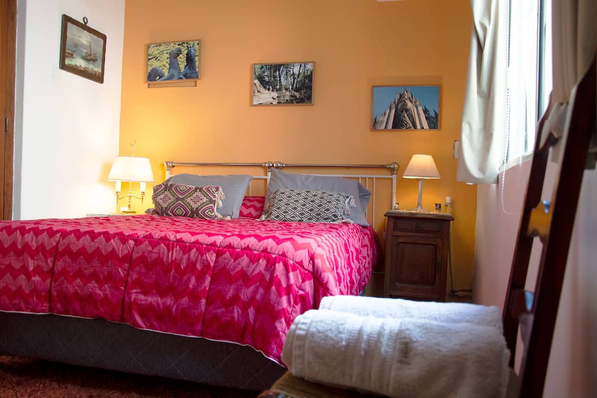 A neatly made bed with a pink and gray patterned bedspread, two bedside lamps, and a wooden nightstand with a lamp.
