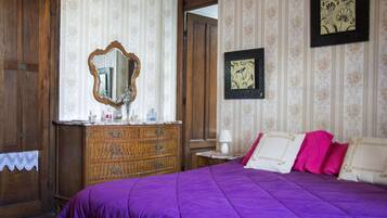 Un dormitorio con un aparador de madera, una colcha morada y un espejo.