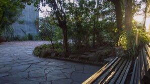 A stone pathway leading to a wooden bench in a park with trees and a concrete wall in the background.