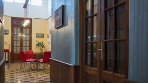 A hallway with a checkered floor, wooden paneling, a red table with chairs, a potted plant, and a door with glass panels.
