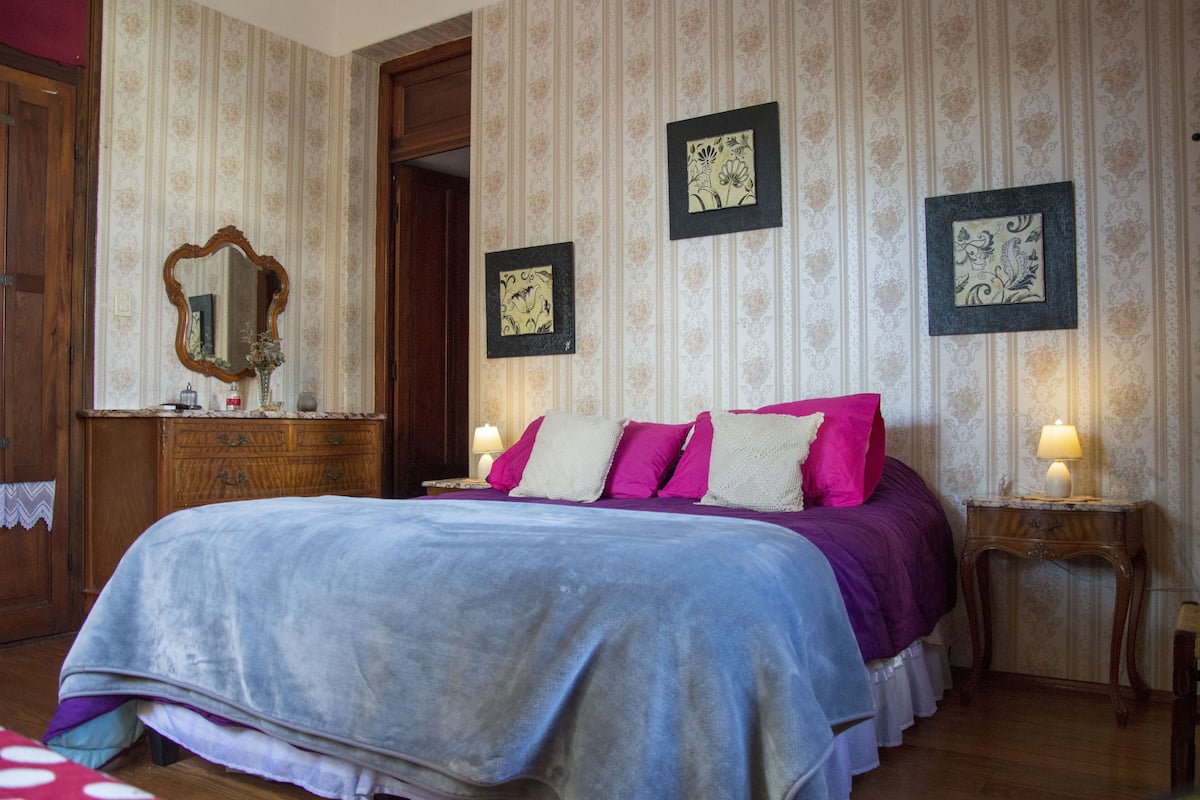 A bedroom with a large bed, wooden dresser, and framed artwork on the walls.