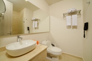 A modern bathroom with a large oval sink, a toilet, a mirror, and a towel rack with towels.