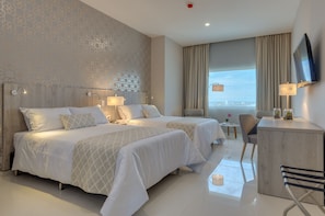 Habitación de hotel con dos camas, un escritorio, una silla, un televisor y vistas a la ciudad.
