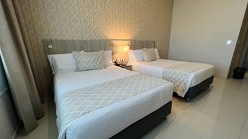 Habitación de hotel con dos camas, una mesita de noche, una lámpara y un papel tapiz estampado.