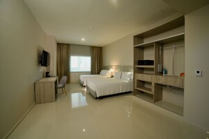 Habitación de hotel con dos camas, un escritorio con silla, televisor, armario y ventana con cortinas.