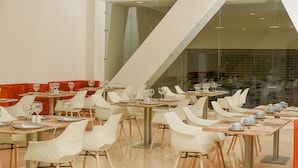 A modern dining area with white chairs and tables, a glass partition, and a staircase. - Hotel Dorado Plaza Alto Prado (Barranquilla)
