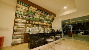 A modern bar area with a curved shelving unit displaying various bottles and glasses, a black marble counter, and three bar stools. - Hotel Dorado Plaza Alto Prado (Barranquilla)