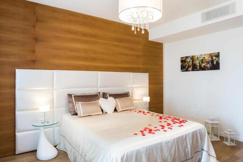 Ein Schlafzimmer mit einem großen Bett, zwei Nachttischen, einer Kristallleuchtre und einem Gemälde an der Wand.