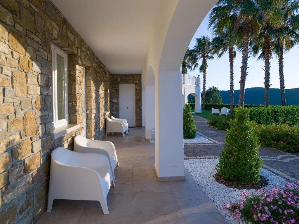 A stone building with white chairs and a pathway leading to a palm tree.