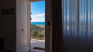 A room with a door leading to a balcony with a view of the sea and a distant cityscape. - La Frescura del Principe (Agropoli)