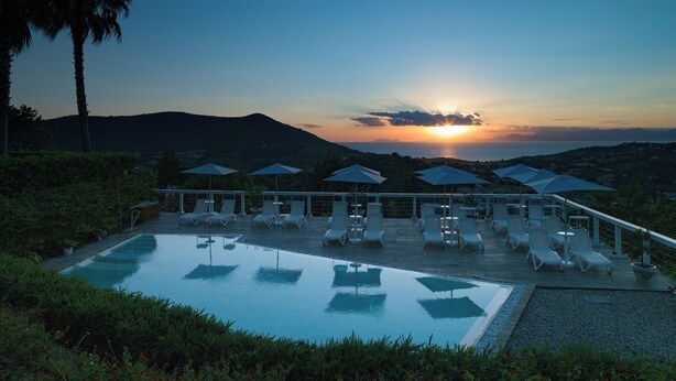 A poolside area with lounge chairs and umbrellas, overlooking a sunset over a mountainous landscape. - La Frescura del Principe (Agropoli)