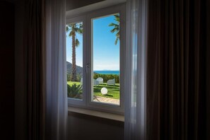 Una ventana con vista a un jardín cuidado, que incluye una palmera y un objeto blanco y esférico en el césped.
