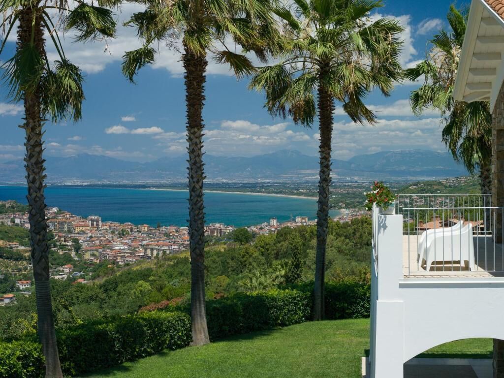 Un balcon avec vue sur une ville côtière, des palmiers et un ciel dégagé.