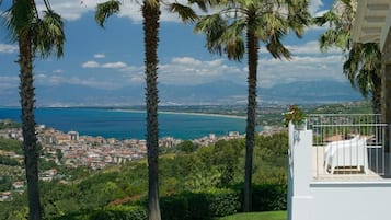 Un balcon avec vue sur une ville côtière, des palmiers et un ciel dégagé.