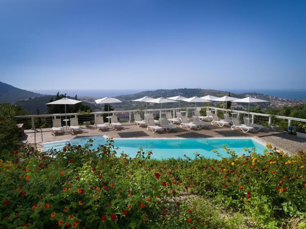 A pool area with lounge chairs and umbrellas, surrounded by greenery and a view of the landscape.