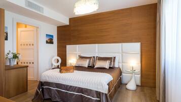 Quarto moderno com cabeceira de madeira, cama com roupa de cama branca e castanha, mesas de cabeceira com luminárias e chão de madeira.