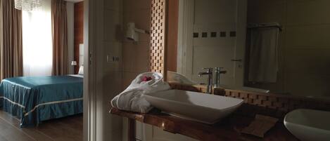 A hotel room with a bed, a bathroom with a sink and mirror, and a shower.