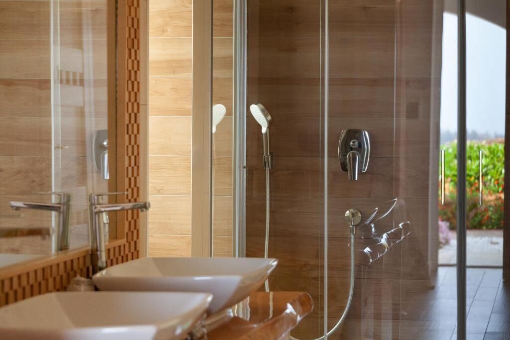 A modern bathroom with a glass shower enclosure, a wooden accent wall, and a view of greenery outside.