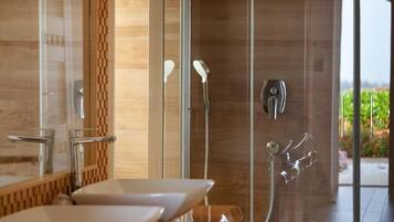 A modern bathroom with a glass shower enclosure, a wooden accent wall, and a view of greenery outside.