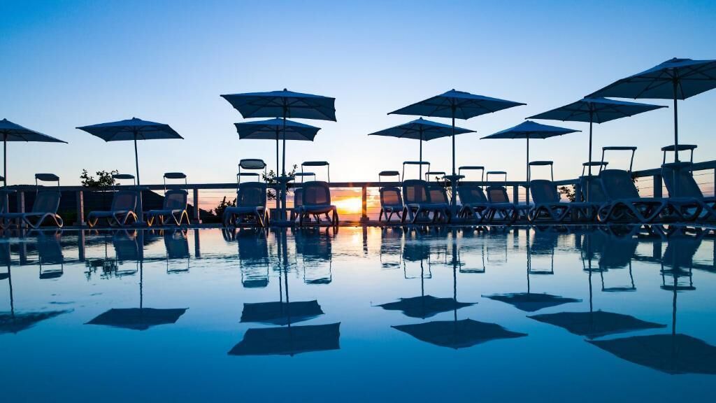 A poolside area with lounge chairs and umbrellas, reflecting the pool's surface.