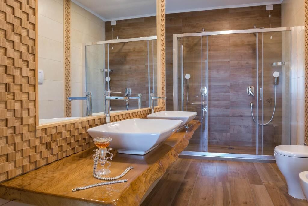Une salle de bain moderne avec un meuble-lavabo en bois, deux vasques, une douche en verre et des toilettes.