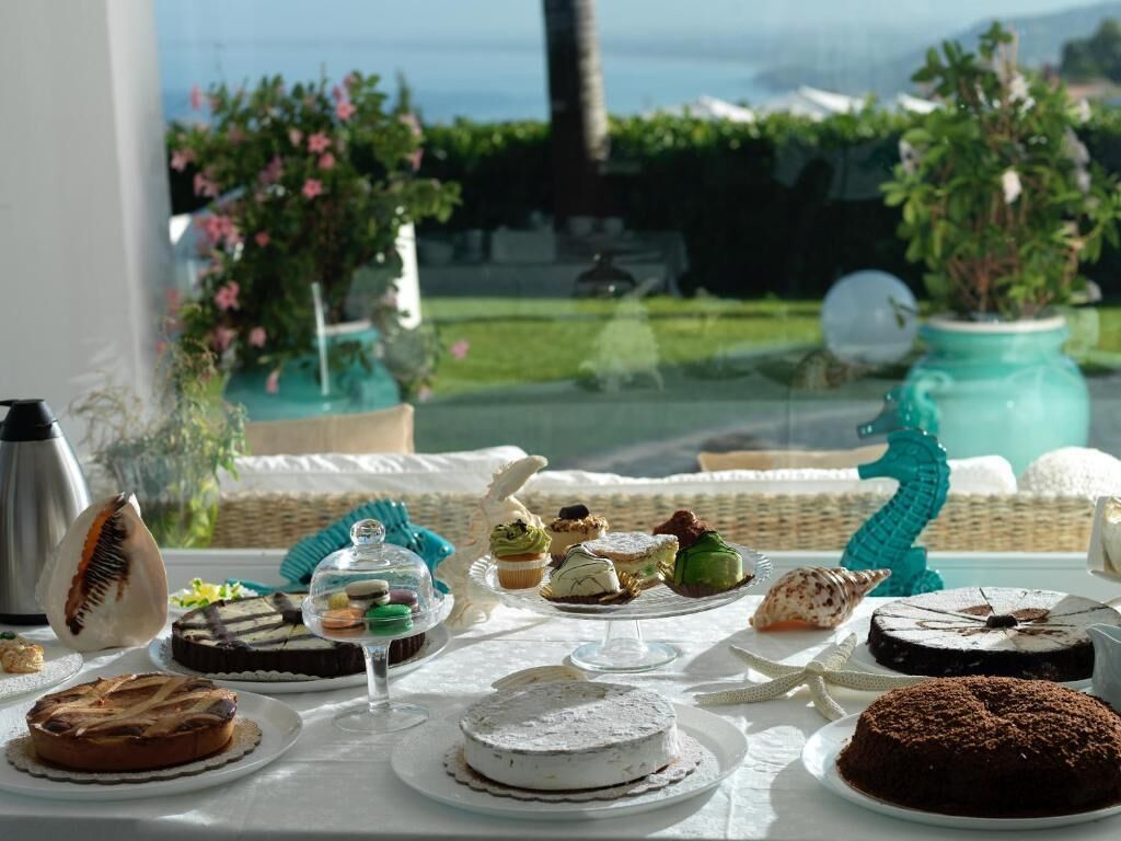 A table set with various desserts and pastries, a coffee pot, and a decorative teal sculpture.