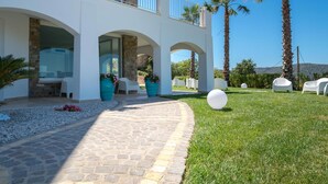 A modern villa with a stone pathway leading to a covered outdoor seating area, surrounded by palm trees and a clear blue sky. - La Frescura del Principe (Agropoli)