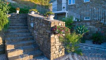 A stone staircase leading to a house with a balcony, surrounded by potted plants and flowers.