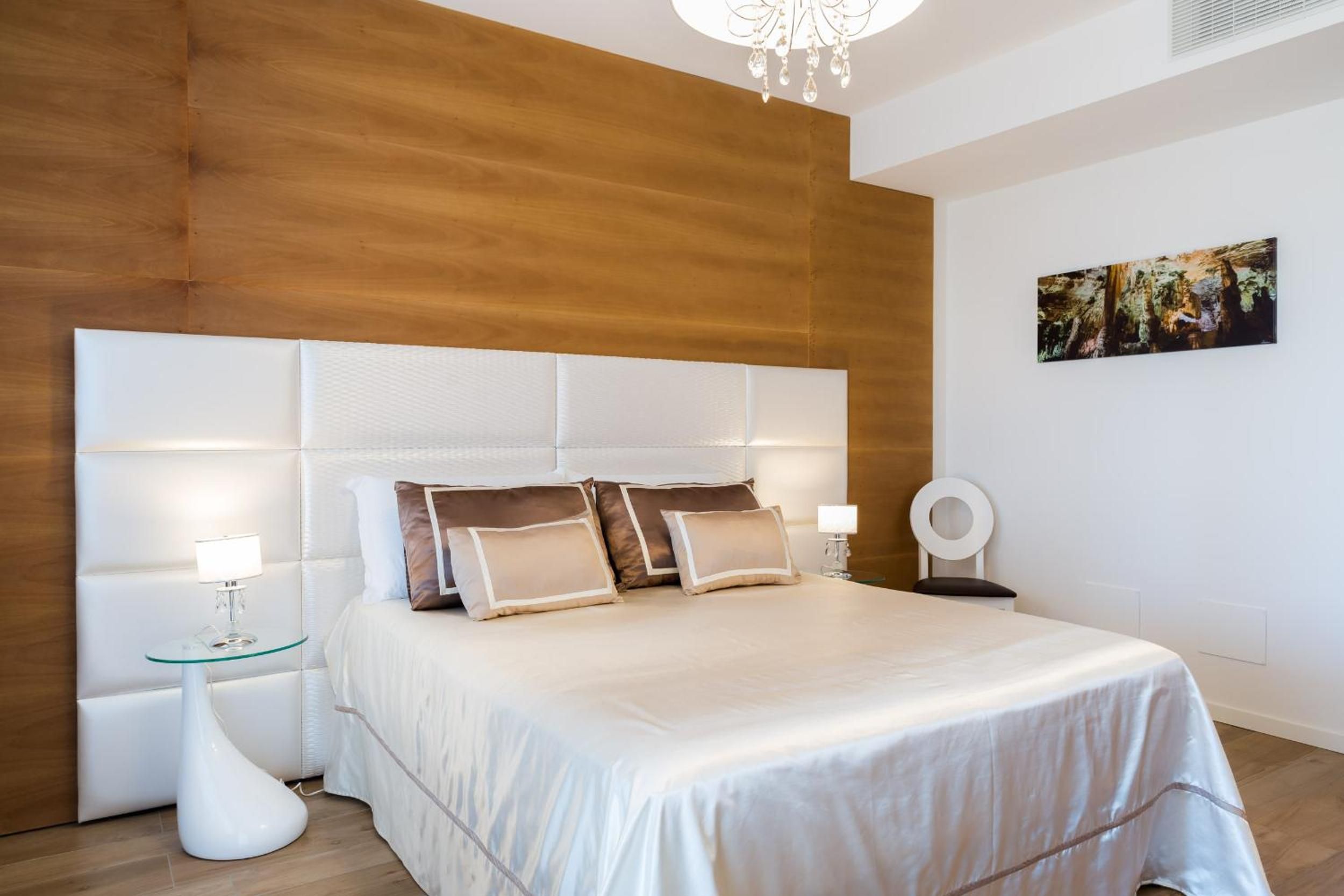 Un dormitorio moderno con una cama grande, dos mesitas de noche, una araña y un cuadro en la pared.