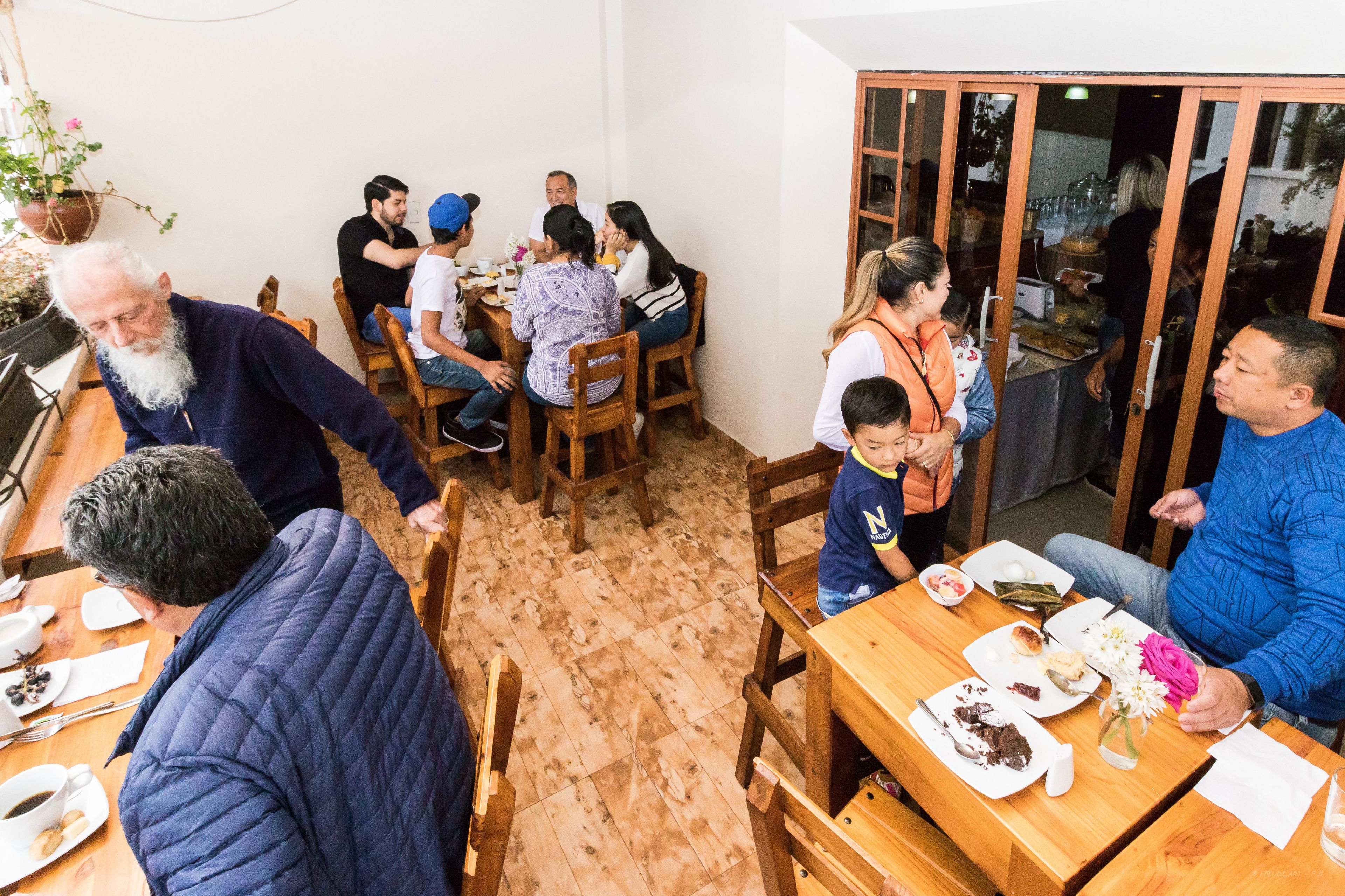 Un comedor con mesas y sillas de madera, una planta en maceta y un ventanal corredizo que da a un espacio exterior.