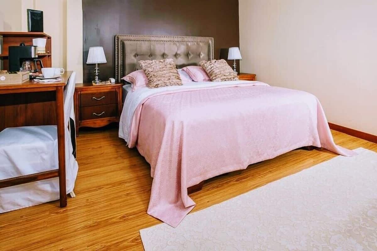 Un dormitorio con una cama grande, un escritorio con silla, una mesita de noche y una lámpara.