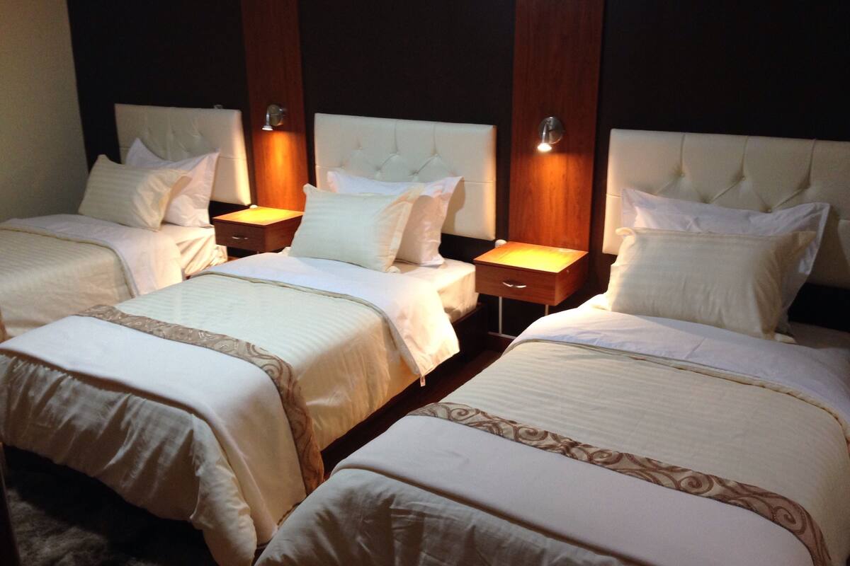 Habitación de hotel con tres camas, cada una con cabecero de madera y lámparas de noche.