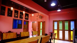 A dining area with wooden benches and tables, a fan, and artwork on the walls. - Nap Corner Hostel (Phitsanulok)