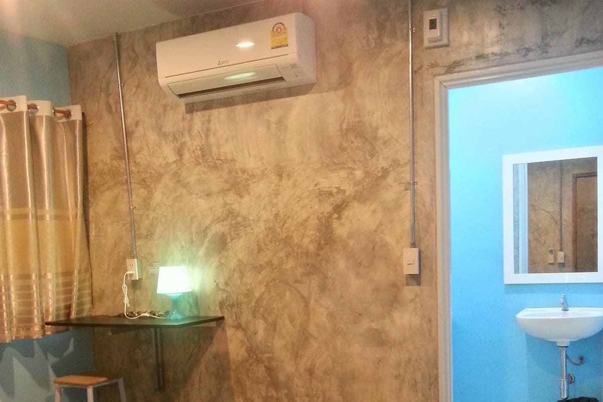 A room with a bed, a desk, a chair, an air conditioner, a mirror, and a bathroom with a sink and toilet.
