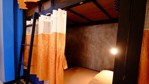 A single bunk bed with a ladder, orange patterned curtains, and a bedside lamp. - Nap Corner Hostel (Phitsanulok)