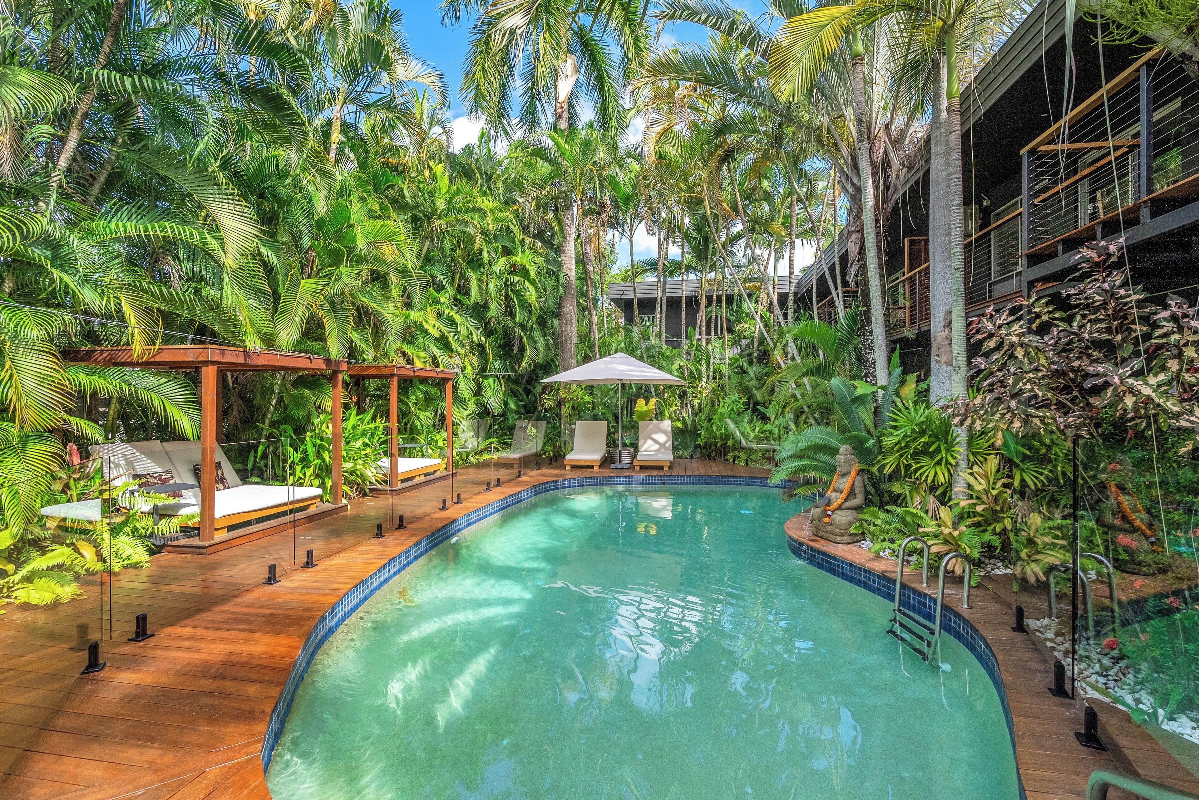 A pool area with lounge chairs, a pergola, and lush tropical vegetation.
