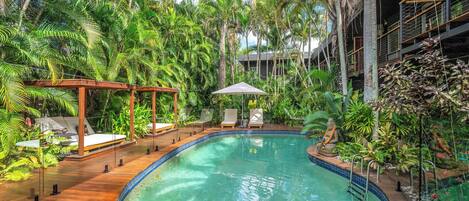 A pool area with lounge chairs, a pergola, and lush tropical vegetation.